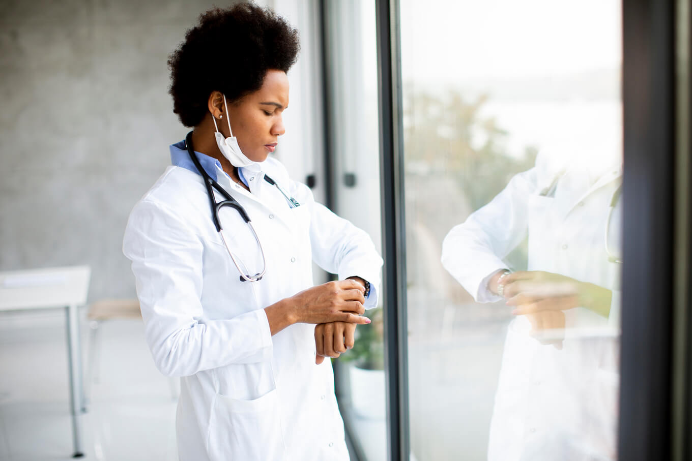 Médica em pé junto à janela do consultório médico e verificando o tempo no relógio